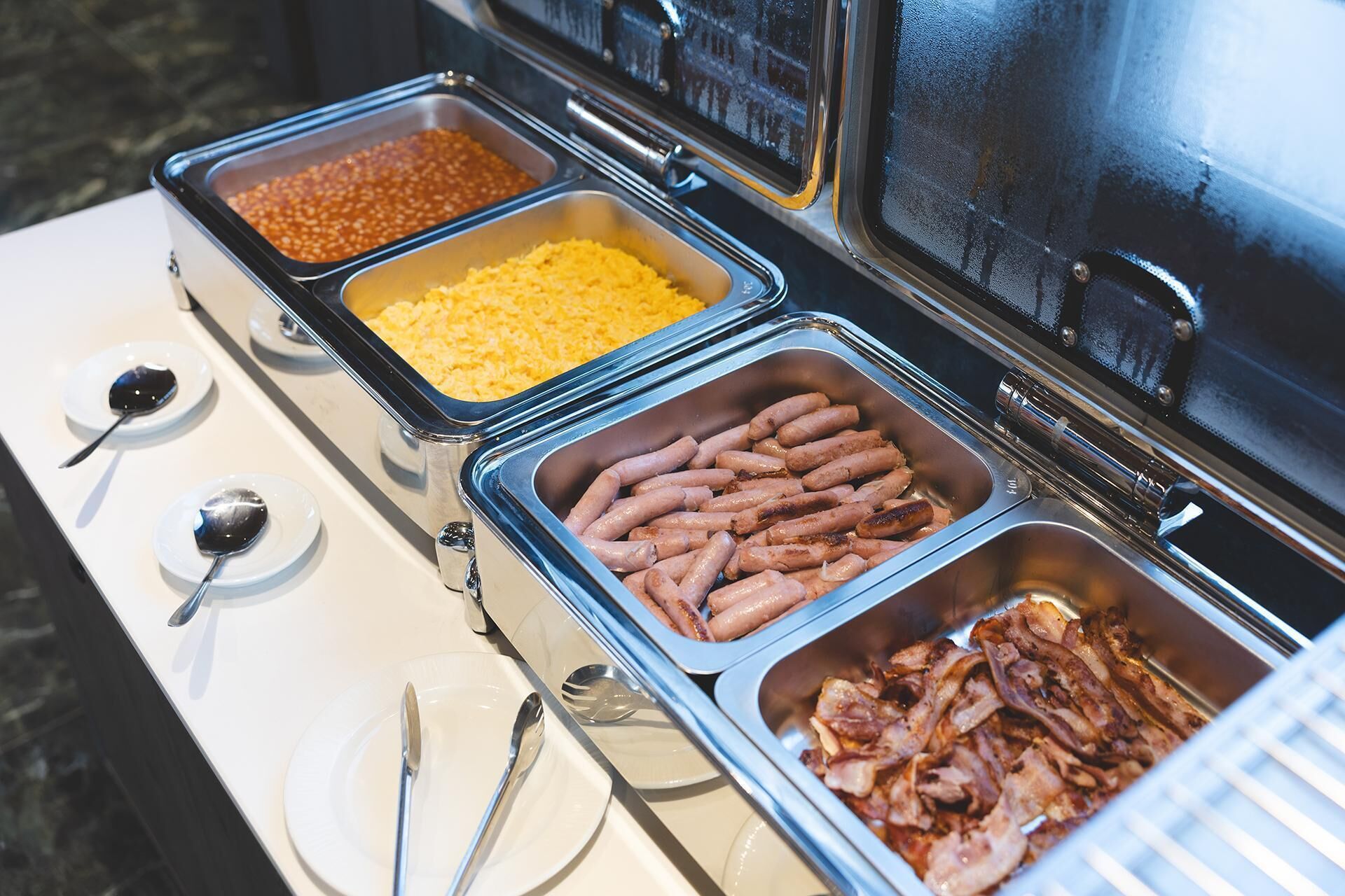 Ein Buffet mit verschiedenen Speisen, darunter Bohnen, Käse, Würstchen und Speck.