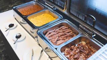 Ein Buffet mit verschiedenen Speisen, darunter Bohnen, Käse, Würstchen und Speck.