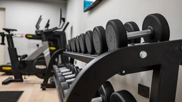 Une salle de sport avec des rangées d’haltères, du matériel d’exercice et un téléviseur accroché au mur.