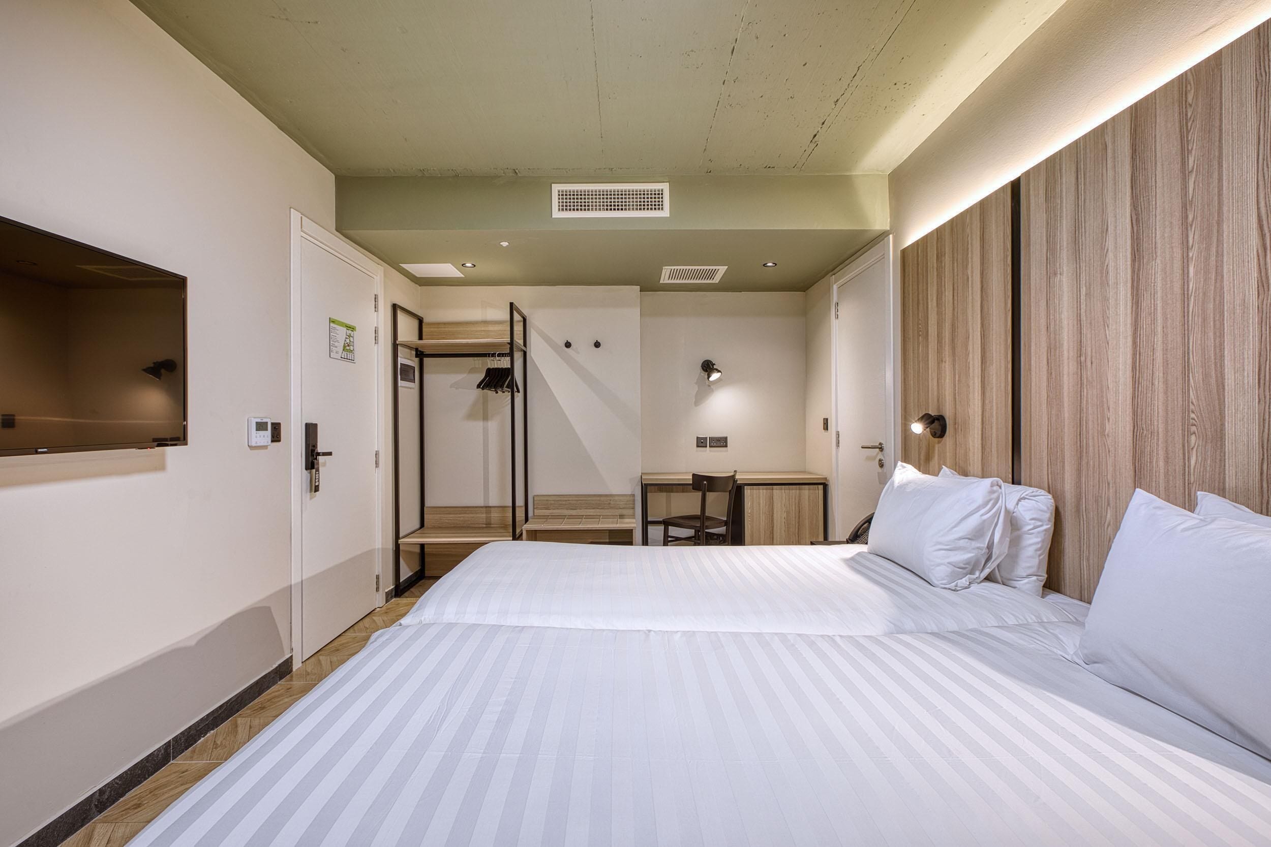 A hotel room with a large bed, a desk, a chair, and a wardrobe.