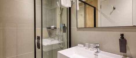 A modern bathroom with a glass-enclosed shower, a white sink with a mirror above it, and a wooden panel on the wall.