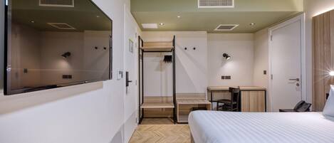 Ein Hotelzimmer mit Bett, Schreibtisch, Stuhl, Kleiderschrank und Spiegel.
