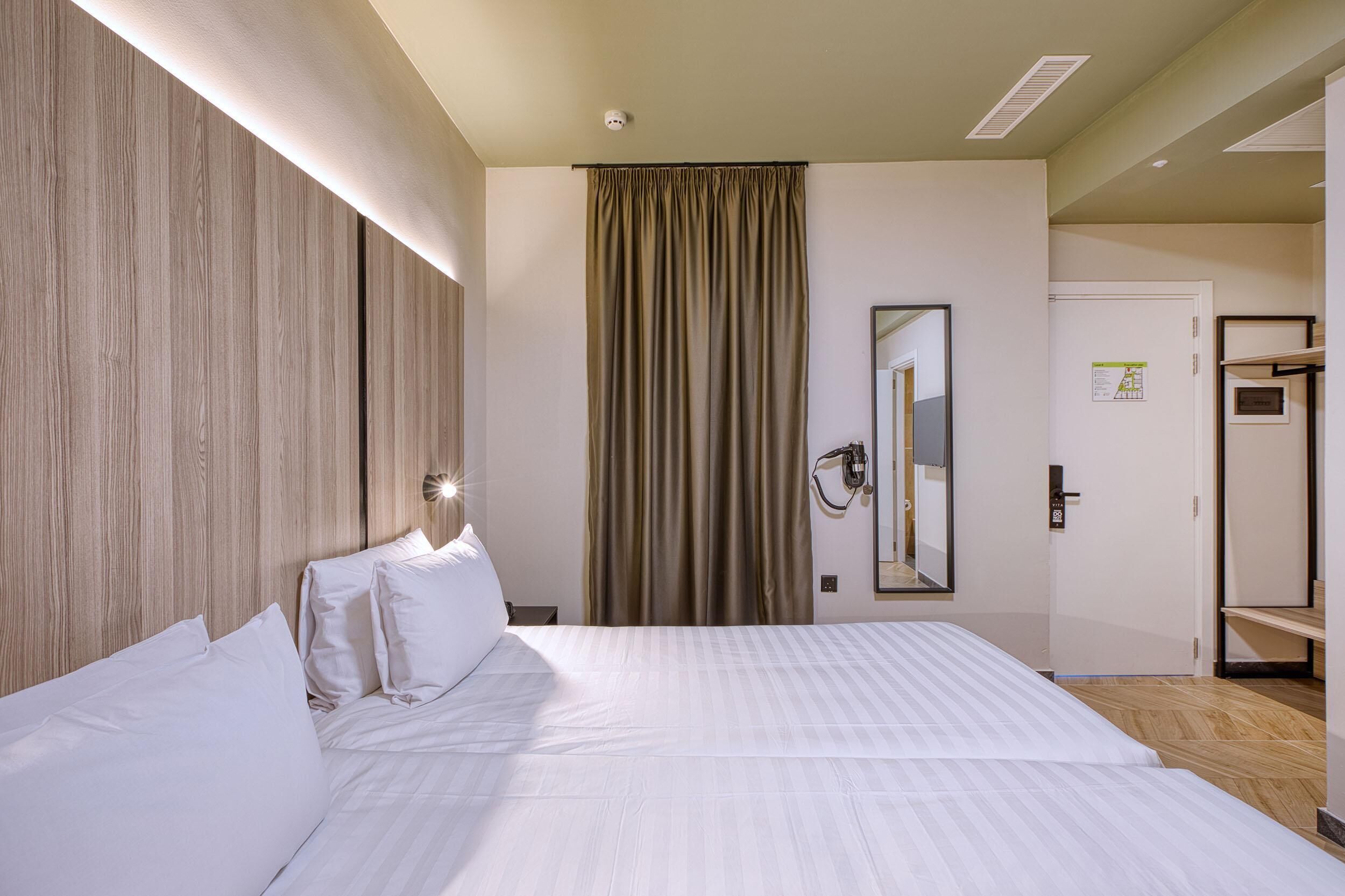 Una camera d'albergo con un letto grande, una testiera in legno, uno specchio, una porta e un lampadario.