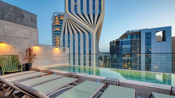 A rooftop pool area with lounge chairs, a modern building with a unique design, and a clear sky. - VITA Hotel (St. Julian's)