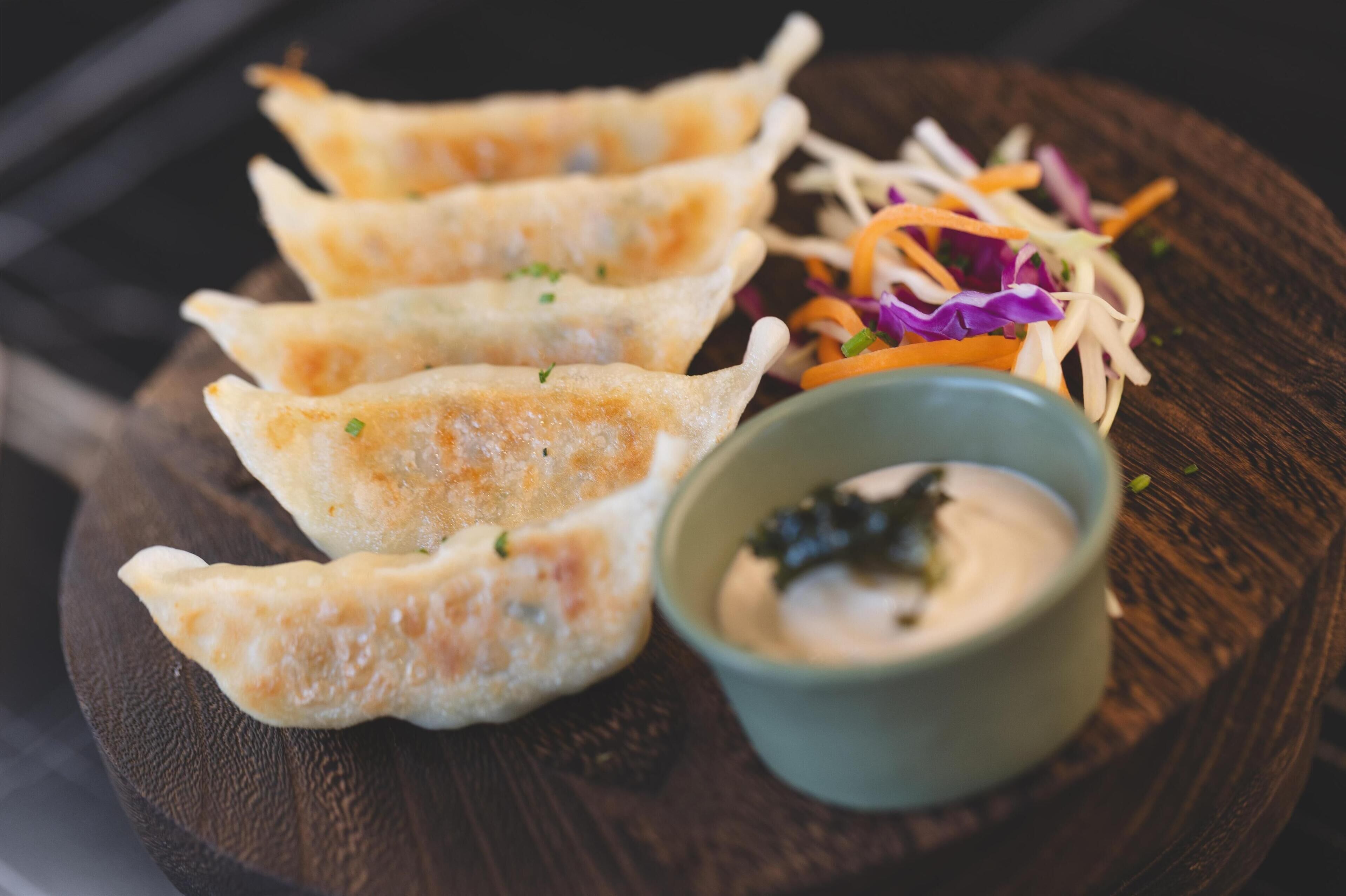 Un plato con cuatro dumplings, una ensalada pequeña y un recipiente con salsa para mojar.