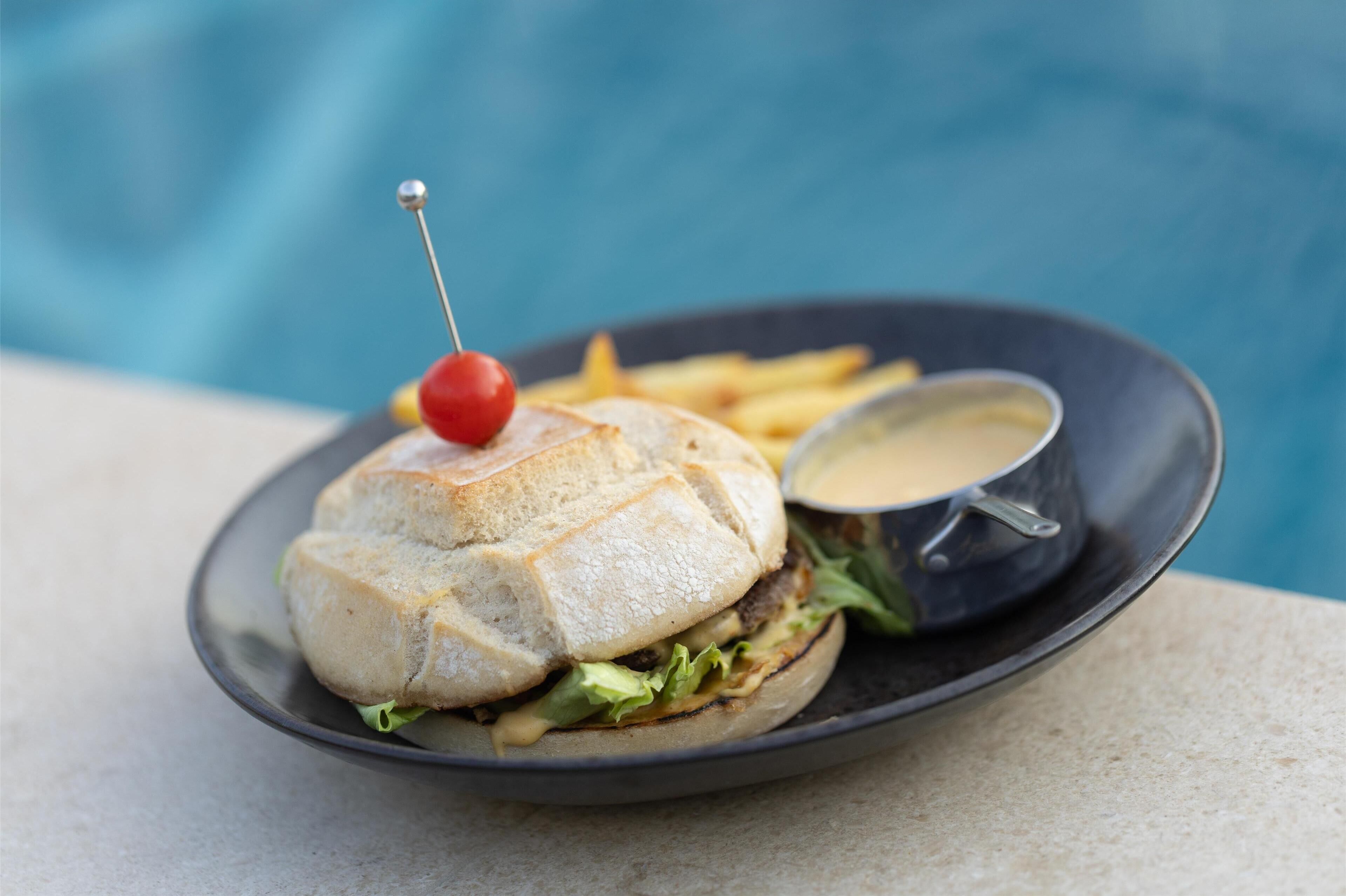 A sandwich with a cherry on top, a side of fries, and a dipping sauce on a plate.