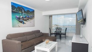 Una sala de estar con un sofá marrón, una mesa de centro blanca y un televisor en la pared.