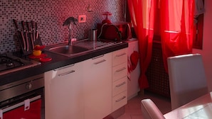 A compact kitchen with white cabinets, a red and white tiled backsplash, a gas stove, and a red kettle.