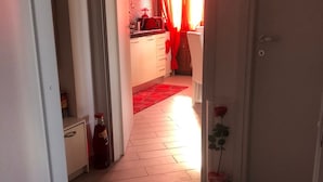 A hallway leading to a kitchen with red curtains and a tiled floor.