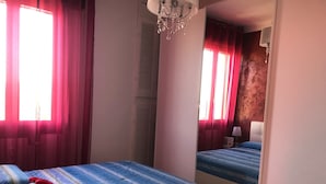 A bedroom with two beds, red curtains, a chandelier, and a mirror.