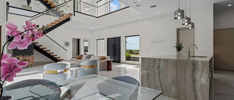 A modern interior with a glass dining table, a staircase, and a kitchen area.