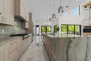 Een moderne keuken met marmeren aanrechtbladen, houten kastjes en hanglampen.