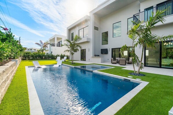 Una casa moderna con piscina, mobiliario exterior y un césped bien cuidado.