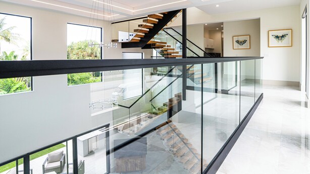 A modern interior with a glass railing, a wooden staircase, and a view of a garden. - SOL HAUS! LUXE NEW 6 BDRM BEACH HOUSE W/ STUNNING VIEWS/POOL/SPA/PUTTING GRN/GYM (Juno Beach)
