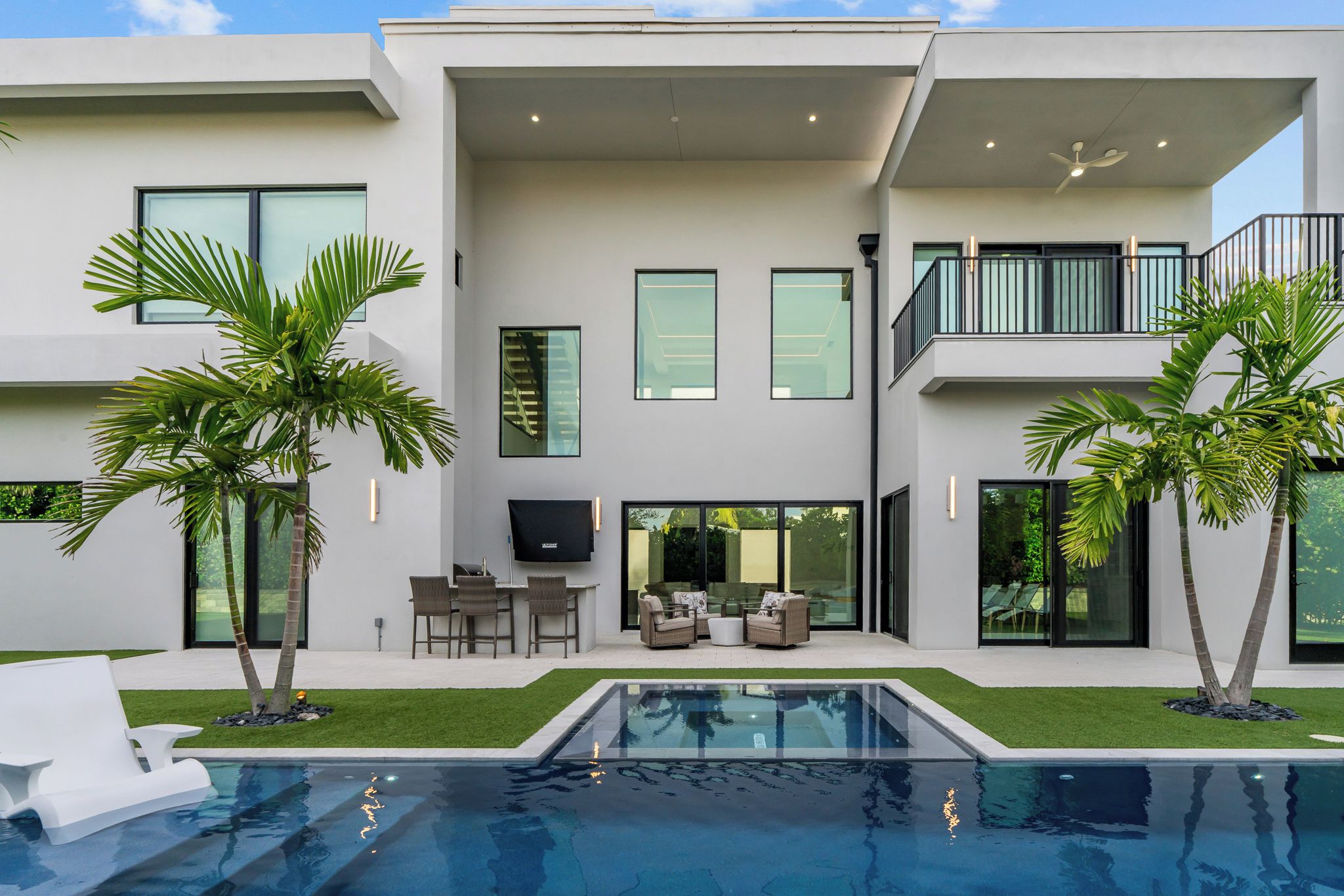 Et moderne hus med to etager, en swimmingpool, udendørs møbler og et fladt tag.