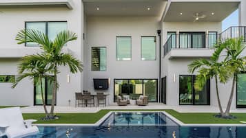 Et moderne hus med to etager, en swimmingpool, udendørs møbler og et fladt tag.