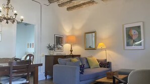 Un salon comprenant un canapé, une table à manger avec des chaises, un lustre et un plafond avec des poutres apparentes.
