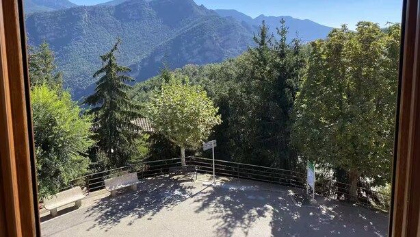 Une vue depuis une fenêtre donnant sur un paysage montagneux, avec des arbres et un banc.