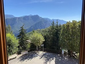 A view from a window overlooking a mountainous landscape with trees and a bench.