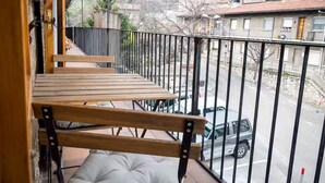 Un balcon doté de bancs en bois et d’un siège rembourré, donnant sur une rue bordée de voitures garées et d’immeubles.