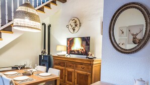 Een eetruimte met een houten tafel gedekt voor vier personen, een televisie waarop een haard te zien is, en een hond die op de vloer zit.