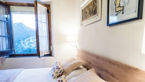 Een slaapkamer met een houten hoofdbord, een bed met gekleurde kussens, een raam met uitzicht op bergen en een lijst met een foto aan de muur.