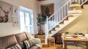 Een gezellige woonkamer met een bruine leren bank, een eettafel gedekt voor vier personen, en een trap met witte leuningen.