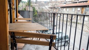 Een balkon met houten trap en een comfortabele bank, met uitzicht op een straat met geparkeerde auto's en gebouwen.