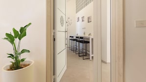 A hallway with a potted plant, a white door, a table with chairs, and a tiled wall with pictures. - Liberty Barocco - Matrimoniale Piccola (Lecce)