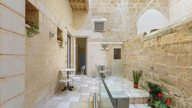 A narrow stone courtyard with a glass railing, white metal chairs, and potted plants. - Liberty Barocco - Matrimoniale Piccola (Lecce)