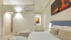 A hotel room with a bed, a wall-mounted air conditioner, a painting, and a window with a view. - Liberty Barocco - Matrimoniale Piccola (Lecce)