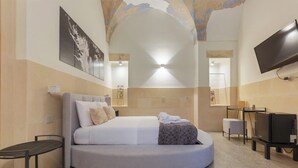 A modern bedroom with a curved bed, a flat-screen TV, and a large painting on the wall. - Liberty Barocco - Suite Deluxe (Lecce)