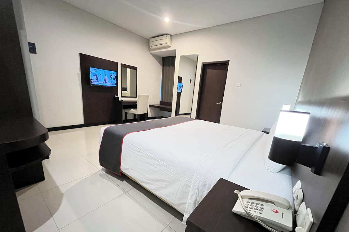 A hotel room with a bed, a desk with a telephone, a TV, and a mirror.