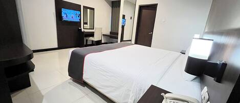 A hotel room with a bed, a desk with a telephone, a TV, and a mirror.