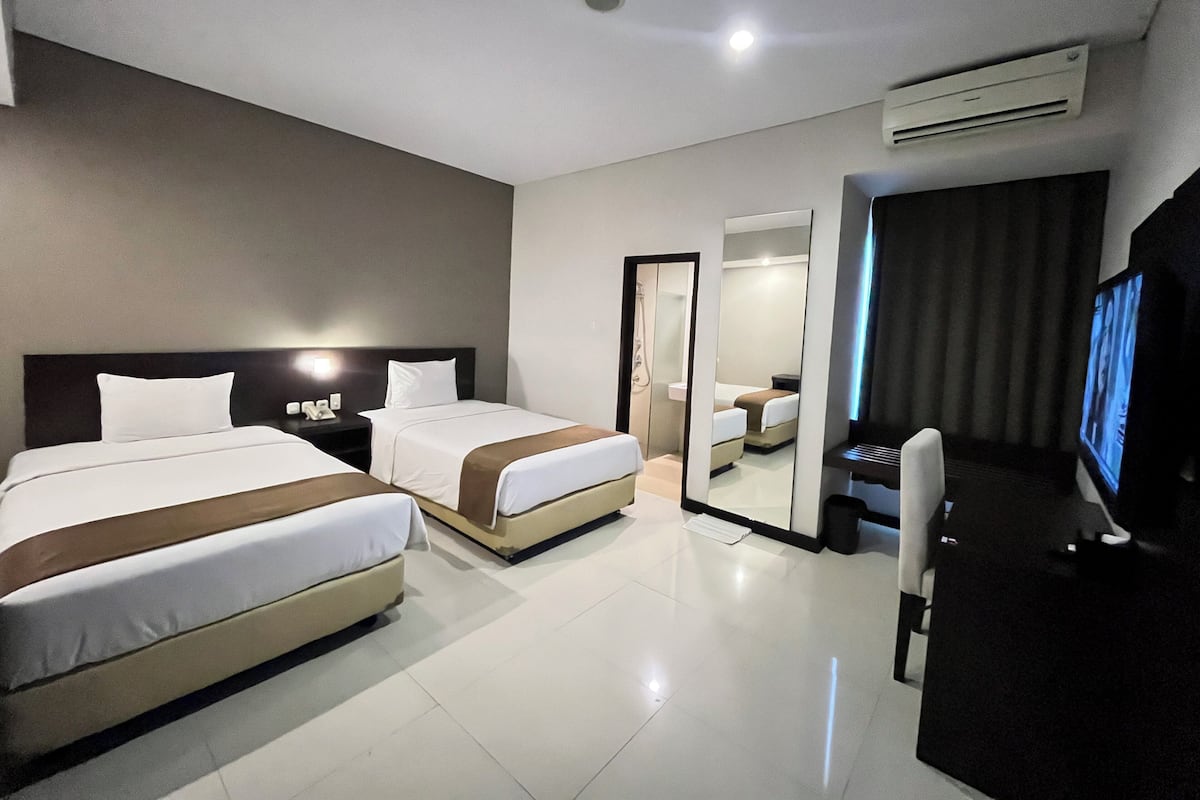 A hotel room with two beds, a desk, a TV, and a mirror.