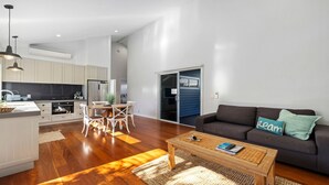A modern living space with a kitchen, dining area, and a sofa with a 'Learn' pillow. - Sawtell Beach Shack 2 (Sawtell)