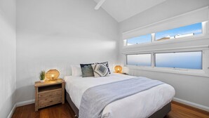 A bedroom with a bed, two bedside tables, a nightstand, and a large window with a view. - Sawtell Beach Shack 2 (Sawtell)