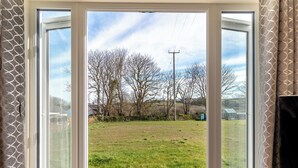 Une pièce dotée d’une grande porte-fenêtre coulissante qui donne sur un espace extérieur verdoyant, avec des arbres et une ligne électrique.