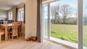 Une cuisine spacieuse dotée d’appareils électroménagers modernes, un coin repas avec des meubles en bois et de grandes portes-fenêtres coulissantes donnant sur un espace extérieur verdoyant.