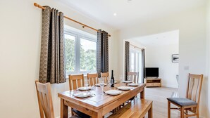 Un coin repas avec une table en bois dressée pour quatre personnes, un banc et des rideaux aux fenêtres.