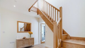 Un escalier en bois avec une rampe, une console en bois ornée d’un vase de tournesols et un miroir accroché au mur.