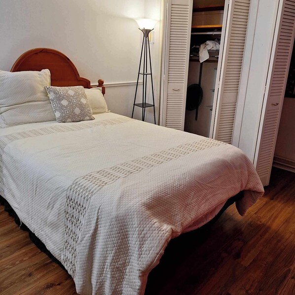 A bedroom with a wooden bed, white bedding, a floor lamp, and a closet with sliding doors. - 2 bedroom semi- duplex (Sydney)