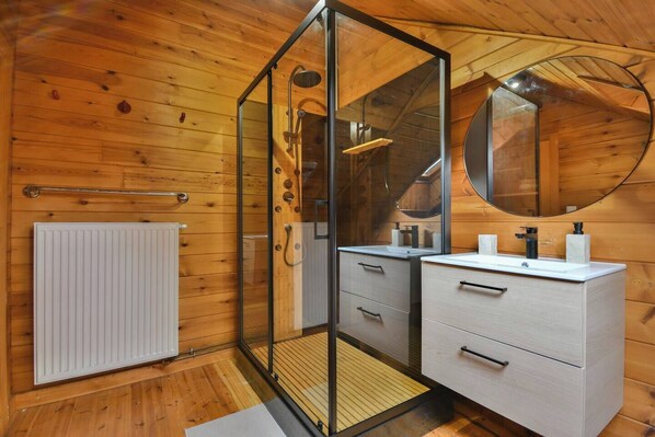 Ein modernes Badezimmer mit Holzwänden, einer Duschkabine aus Glas, einem weißen Handtuchwärmer und einem runden Spiegel über dem Waschbecken.