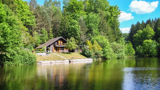 Une cabane au bord d’un lac, entourée d’une forêt dense.