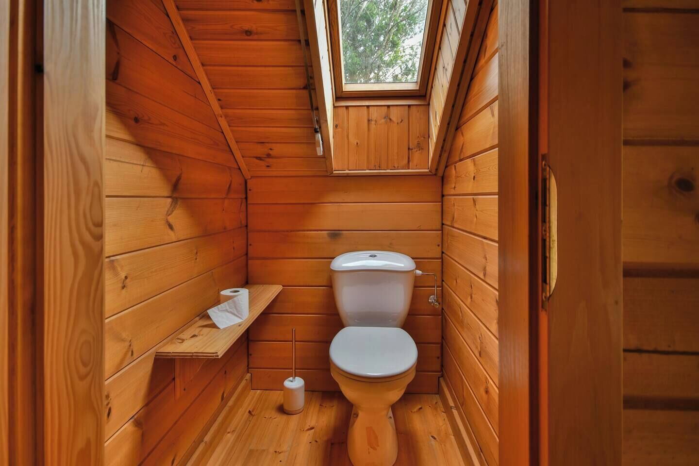 Ein kleines Badezimmer in einer Holzhütte mit einer Dachfenster, einer Toilette und einem Holzregal mit einer Toilettenpapierrolle.