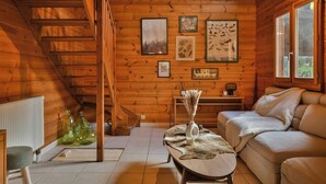 L’intérieur d’un chalet accueillant, avec un escalier en bois, un canapé, une table basse et des tableaux encadrés accrochés aux murs.