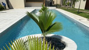 Une piscine agrémentée d’un élément décoratif circulaire en pierre et d’un palmier au premier plan.