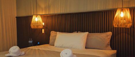 A hotel room with a large bed, two pillows, two rolled towels, and two wall-mounted lamps.