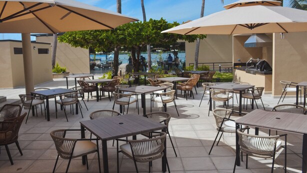 Un espace extérieur aménagé en terrasse, avec des tables et des chaises, des parasols et une vue sur la mer.