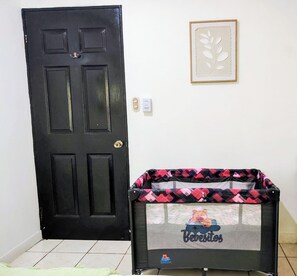 Une porte noire avec un trou de serrure, une œuvre d’art encadrée accrochée au mur et un sac de transport pour animaux avec un motif d’ours posé sur le sol.